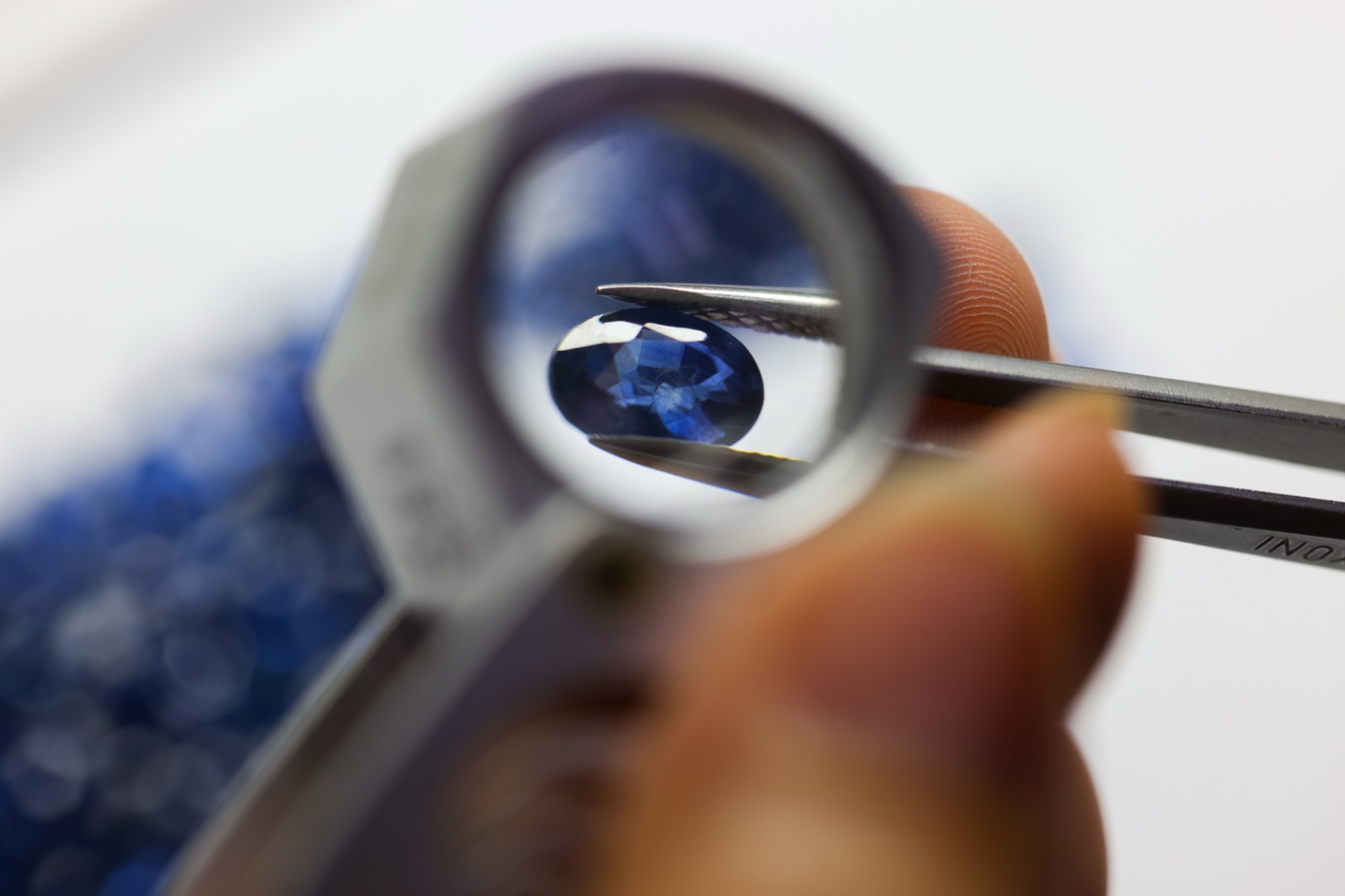 Blue sapphire held in tweezers, inspected through a loupe
